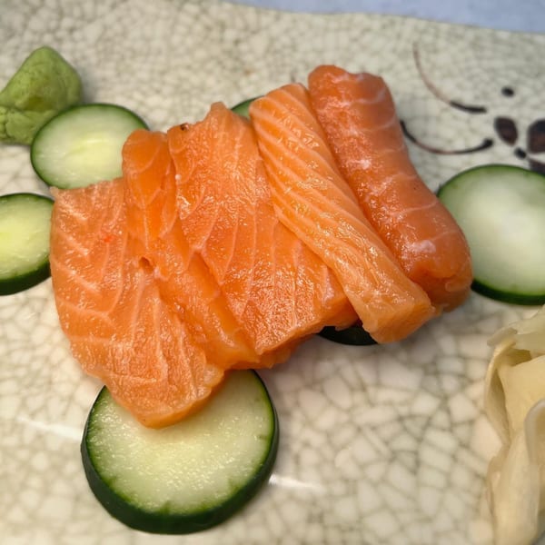 Shinrai Japanese Bistro's salmon sashimi with cucumber slices, wasabi, and pickled ginger on a patterned plate.
