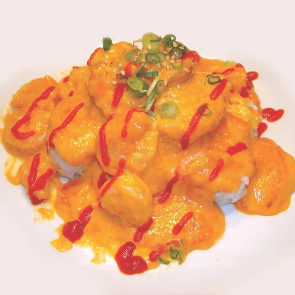 Shinrai Japanese Bistro's volcano roll, topped with bright orange sauce, red drizzle, sesame seeds, and green onions.