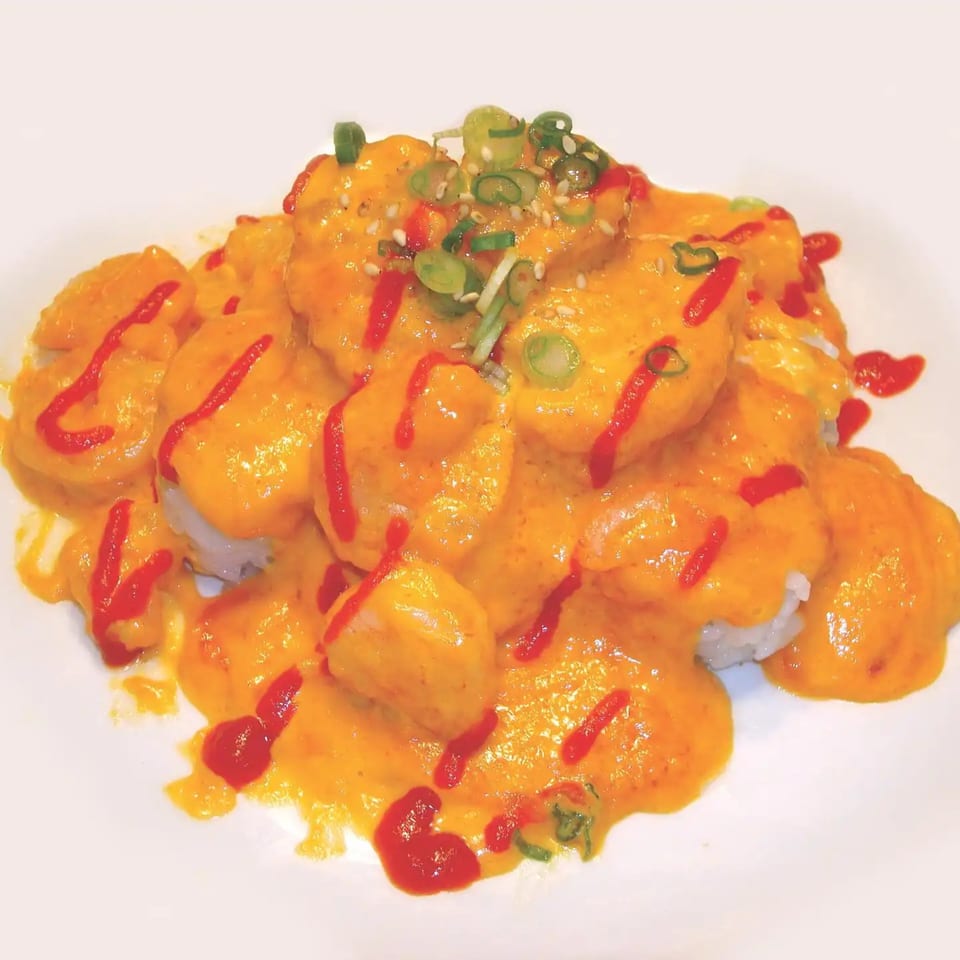 Shinrai Japanese Bistro's volcano roll, topped with bright orange sauce, red drizzle, sesame seeds, and green onions.