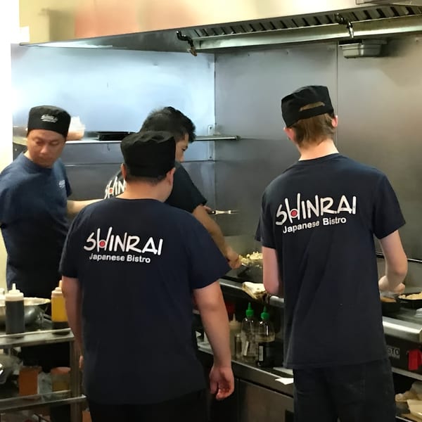 Shinrai Japanese Bistro chefs in black uniforms cooking in a busy kitchen.