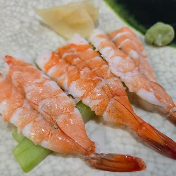 Three pieces of shrimp nigiri sushi with pickled ginger and wasabi on a white plate.