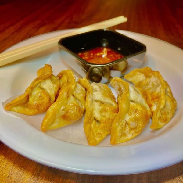 Golden-fried Japanese gyoza dumplings with a side of chili dipping sauce and chopsticks on a white plate.
